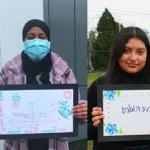 Several students stand with hand drawn signs that say Welcome in different languages.